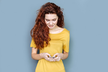 Online interaction. Joyful pretty nice woman smiling and looking at her smartphone screen while...