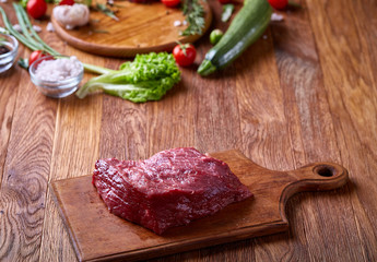 Raw beefsteak on cutting board with vegetables and seasoning, selective focus, close-up, top view