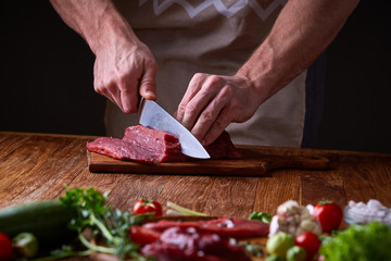 Strong professional man's hands cutting raw beefsteak, selective focus, close-up