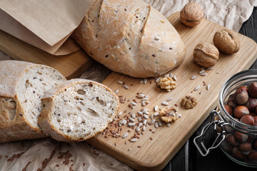 Loaves of gray bread with seeds, in a paper bag, lie on a black table made of wood.