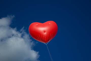 Red heart balloon with smiley face floating against a blue sky.