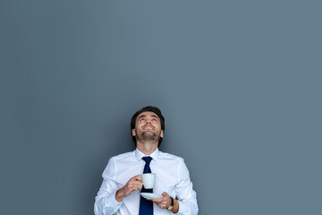 Great mood. Joyful bearded positive man having coffee and looking up while working in the office