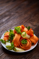 Artistically served vegetable salad with carrot, cucumber, letucce over wooden background, selective focus