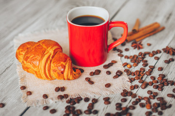  croissants, cinnamon, anise and red mug with black coffee on a wooden table