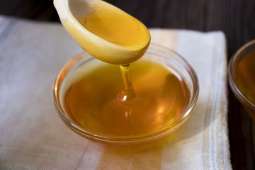 Honey dripping from honey dipper on yellow background. Thick honey dipping from the wooden honey spoon. Healthy food concept, diet, dieting
