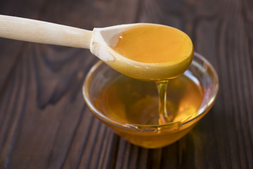 Honey dripping from honey dipper on yellow background. Thick honey dipping from the wooden honey...