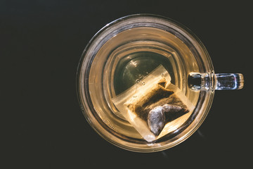Glass cup of tea with bag on dark background