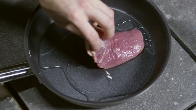 Top view of hand of unrecognizable male cook tossing hot pan with olive oil, then putting piece of raw duck meat and frying it on induction cooktop