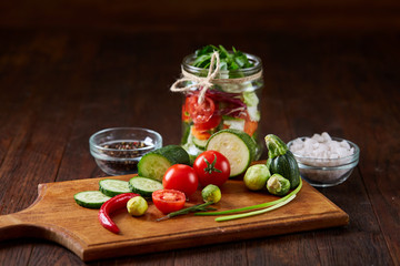 Delicious vegetable salad in jar and fresh veggies on cutting board on table, selective focus, close-up