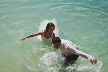Wedding couple is swimming and running in azure blue lake splashes of water. Beautiful bride in...