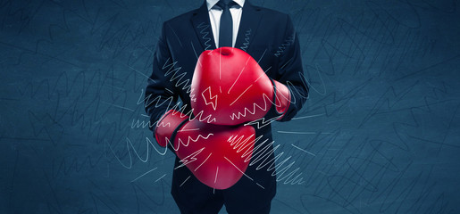 A confident businessman standing in red boxing gloves on his hand in front of blue wall background...