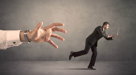 Young miniature businessman running from a big hand with grey background