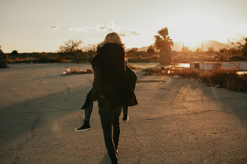 Cool indie couple having fun outdoors while he gives her a piggyback on an abandoned place, during sunset with a beautiful golden light.