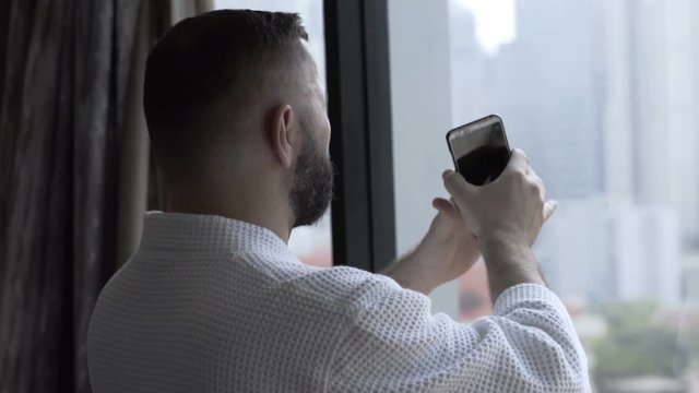 Man in bathrobe doing photos of the city on smartphone
