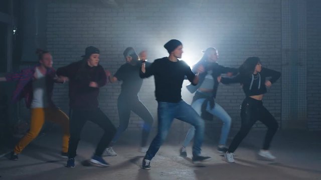 Group of street dancers performing different moves on the dark street.
