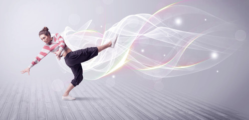 Fototapeta na wymiar A beautiful young hip hop dancer dancing contemporary urban street dance in front of grey wall background with smokey lines and glitter concept.