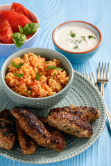 Cevapcici, balkanian grilled meat sausages with savory rice and yogurt dip.