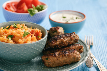 Cevapcici, balkanian grilled meat sausages with savory rice and yogurt dip.