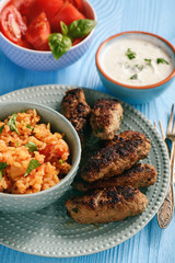 Cevapcici, balkanian grilled meat sausages with savory rice and yogurt dip.
