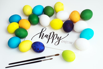 Easter festive colorful eggs on a white background with a greeting card calligraphy "happy easter". eggs yellow, blue, green and blue, orange and purple