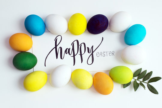Easter festive colorful eggs on a white background with a greeting card calligraphy "happy easter". eggs yellow, blue, green and blue, orange and purple