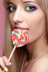Beauty portrait of young blonde woman on pink background. Female with candy lollipop on stick in hands.