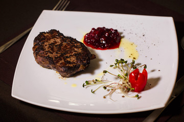 grilled deer steak with tomato and sprouted seeds of radish and cranberry jam on a white plate