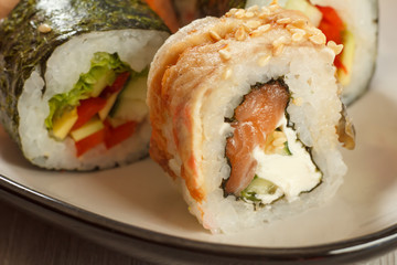 Close up Uramaki with Conger. Sushi rolls with nori, rice, eel fish, cheese, pieces of avocado, cucumber, salmon decorated with sesame seeds and sushi rolls with vegetables on the background
