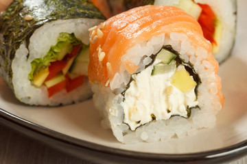 Close up Uramaki Philadelphia. Sushi rolls with salmon, nori, rice, Philadelphia cheese, pieces of avocado, cucumber and sushi rolls with vegetables on the background