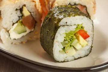 Close up Hosomaki with vegetables. Sushi roll with nori, rice, pieces of avocado, cucumber, red bell pepper and lettuce leaves and  sushi rolls with Conger on the background