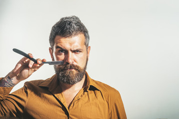 Stylish barber with dangerous razor for shaving in studio. Bearded handsome, sexy macho with...
