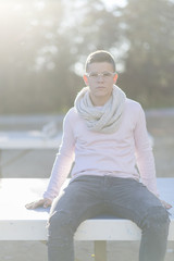 Stylish teenager sitting on a wooden bench on a city park