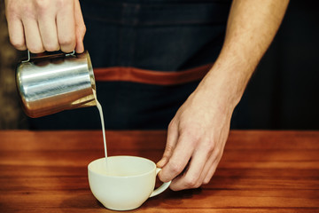 Waiter hands pouring milk making cappuccino