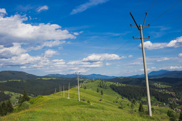 Old rusty power lines at scenic green hills of mountain at bright blue sky background in countryside area. Beautiful scenery summer landscape. Panoramic view of horizon. Horizontal color photo.