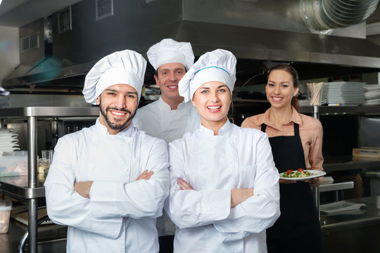Portrait of two confident cheerful chefs in kitchen with staff of restaurant