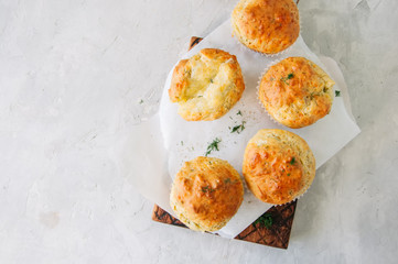 Savory double cheese muffins on a wooden board. White stone background.