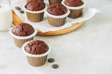 Rich chocolate zucchini muffins on a wooden round plate. White stone background.