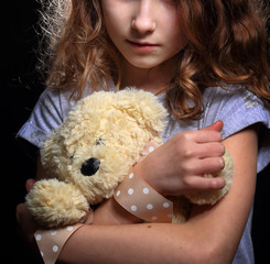 young depressed girl is holding a teddy bear