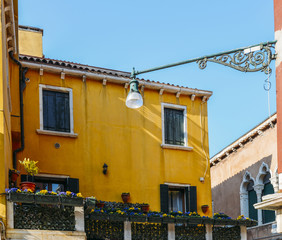 Fototapeta na wymiar Yellow house with flowers and bench. Colorful houses in Burano island near Venice, Italy. Venice postcard. Famous place for european tourism and travel.