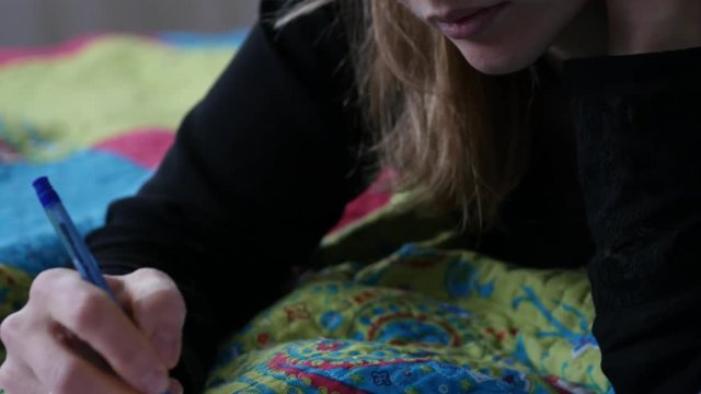 sed young female student lies on a bed and writes in her diary. adolescent experiences. 4K