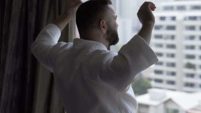 Man in bathrobe stretching muscles in fron of the window
