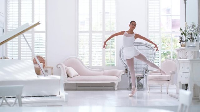 Graceful ballerina practicing ballet in white studio, slow motion