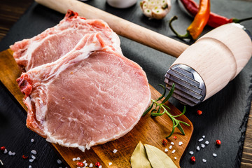 Fresh raw pork chops on black stone on wooden background