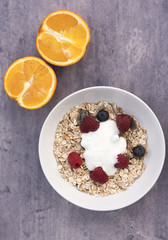 Vertical image of a bowl of Muesli with two orange halves on a blue stone background 