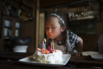 誕生日ケーキのロウソクを吹き消す女の子