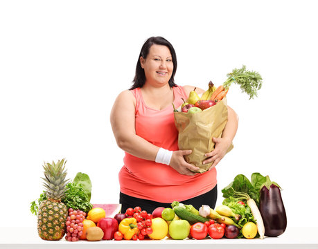 Overweight woman with a groceries bag behind a table with fruit and vegetables