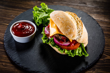 Tasty burger with cheese and ketchup served on black stone
