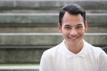 happy man portrait, smiling friendly man, happy handsome man sitting smiling in city environment; young adult south east asian man model with tan skin and short hair