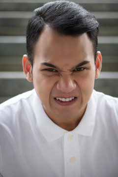 unhappy man portrait, angry man face, hostile handsome man sitting looking at you with bad angry mood emotion; young adult south east asian man model with tan skin and short hair