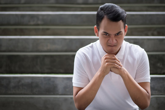 unhappy man portrait, angry man face, hostile man looking at you, clenching fist ready to punch with bad angry mood emotion; young adult south east asian man model with tan skin and short hair